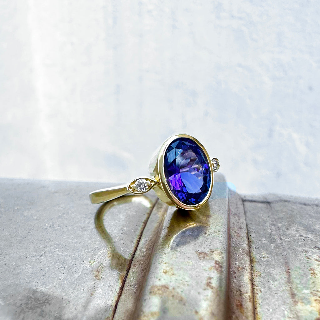 Elegant Oval Bezel Set Tanzanite with Petite Diamond Highlight Yellow Gold Ring